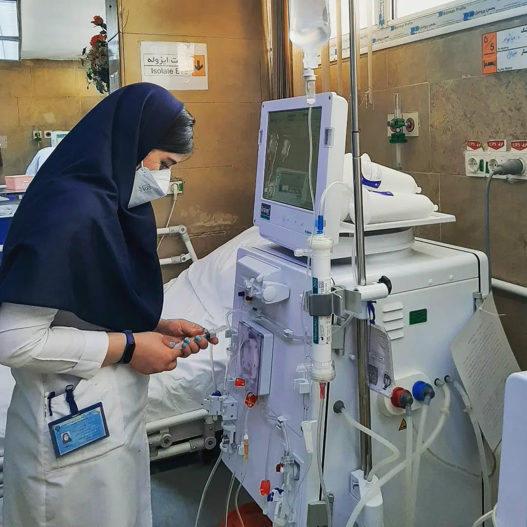 این تصویر محیطی کاملاً بیمارستانی و بالینی را نمایش می‌دهد و نشان می‌دهد که پرستار در حال آماده‌سازی یا پایش دستگاه دیالیز برای بیمار است؛ دستگاه دیالیز، وظیفه تصفیه خون بیماران دارای مشکلات کلیوی را بر عهده دارد